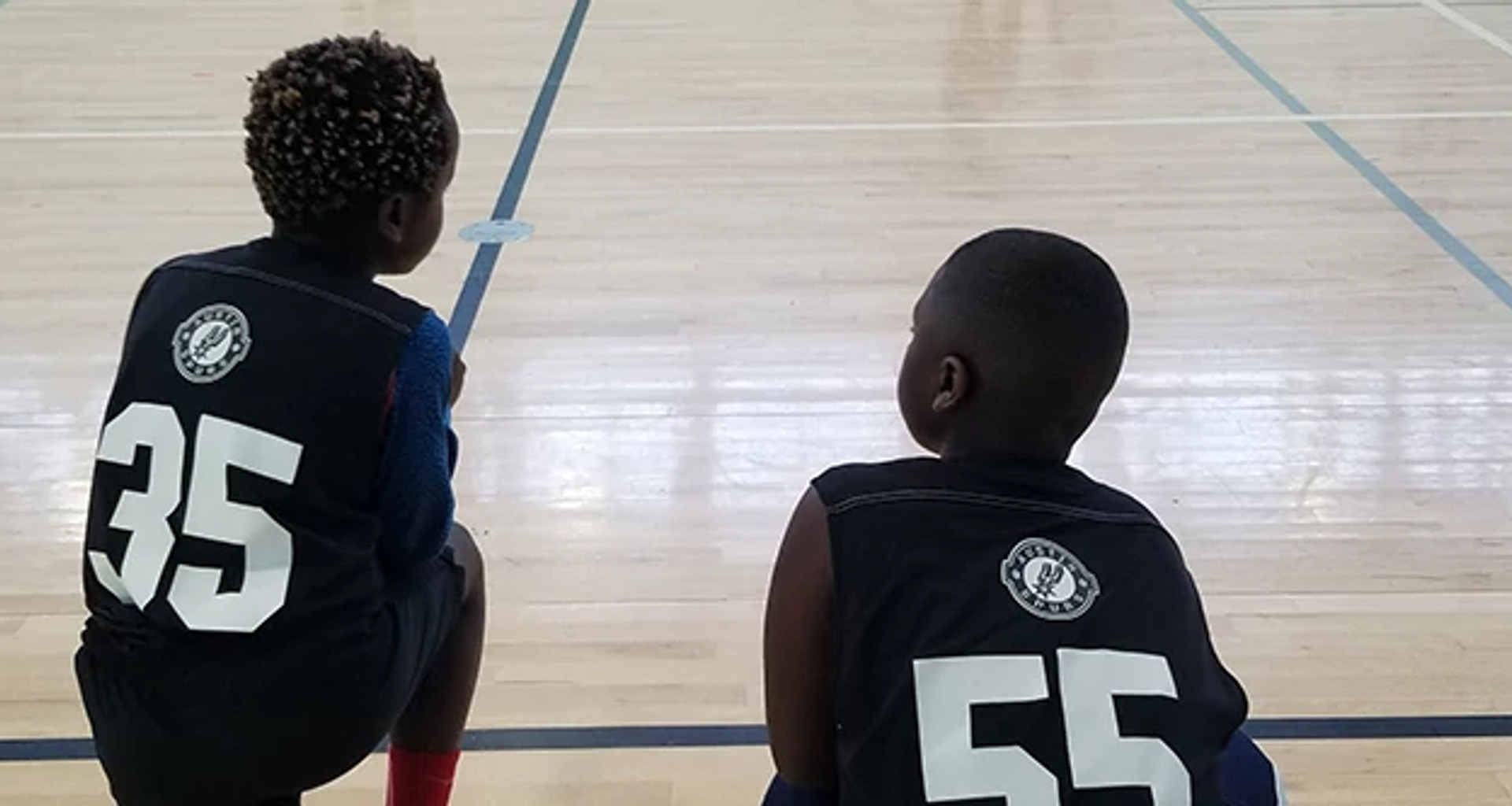 Two kids sitting on edge of basketball court
